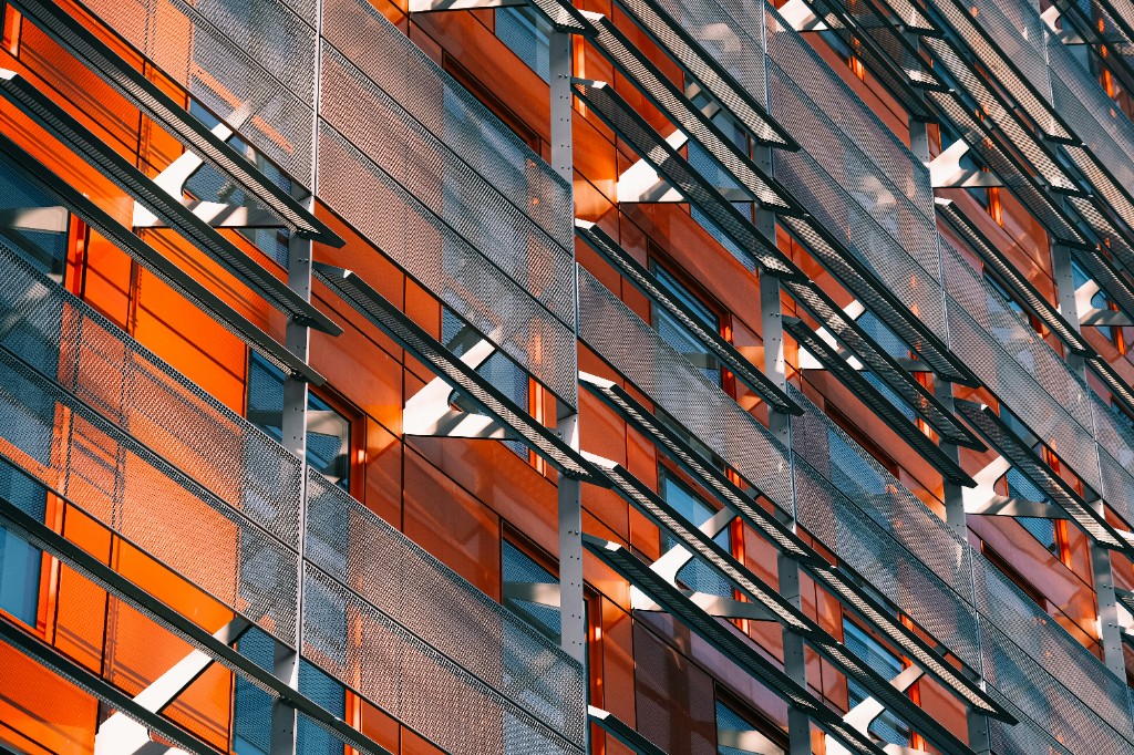 Modern building facade with orange panels, glass windows, and perforated metal sunshades.